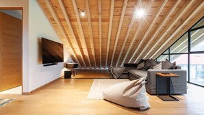 Camera da letto moderna in stile loft con soffitto spiovente, un'ampia finestra, una TV a schermo piatto, un divano e un piccolo tavolo.