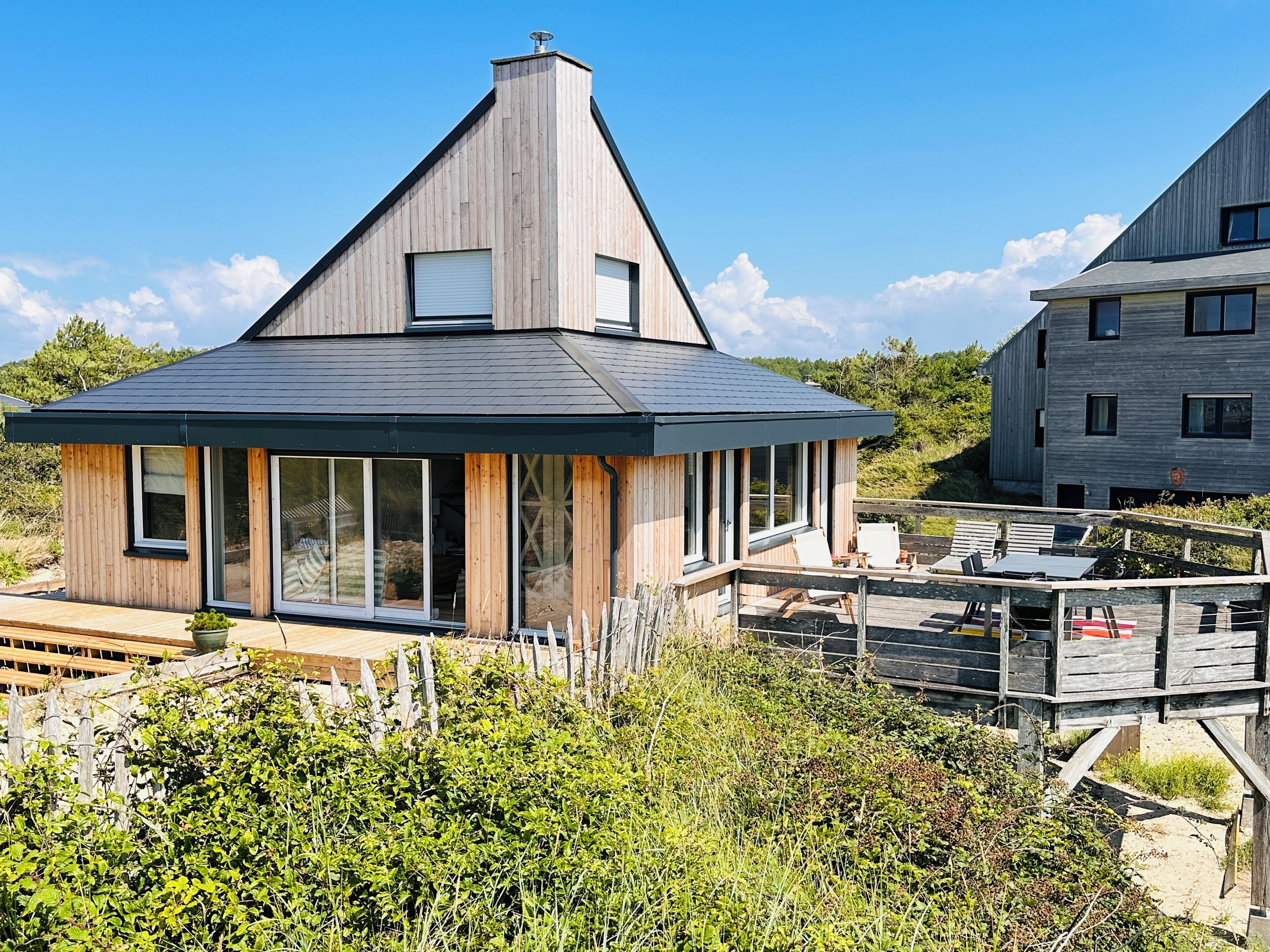A modern house with a sloped roof, large windows, and a deck with outdoor furniture.