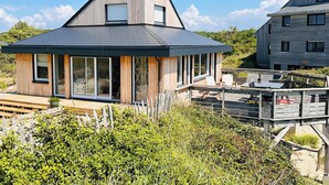 A modern house with a sloped roof, large windows, and a deck with outdoor furniture. - Les Eléments - Quiet, dunes and sandy beach within walking distance - 6 people (Quend)