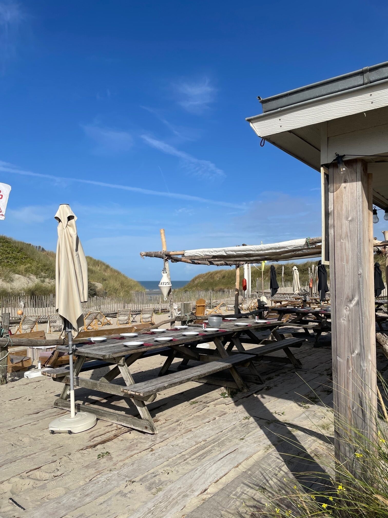 A beachside wooden structure with picnic tables and umbrellas, overlooking the sea.