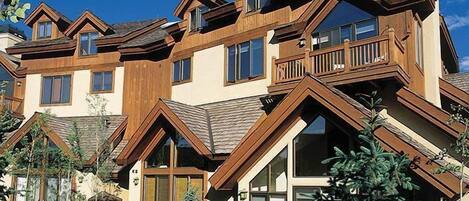 A modern multi-story house with a prominent wooden facade, large windows, and a balcony.