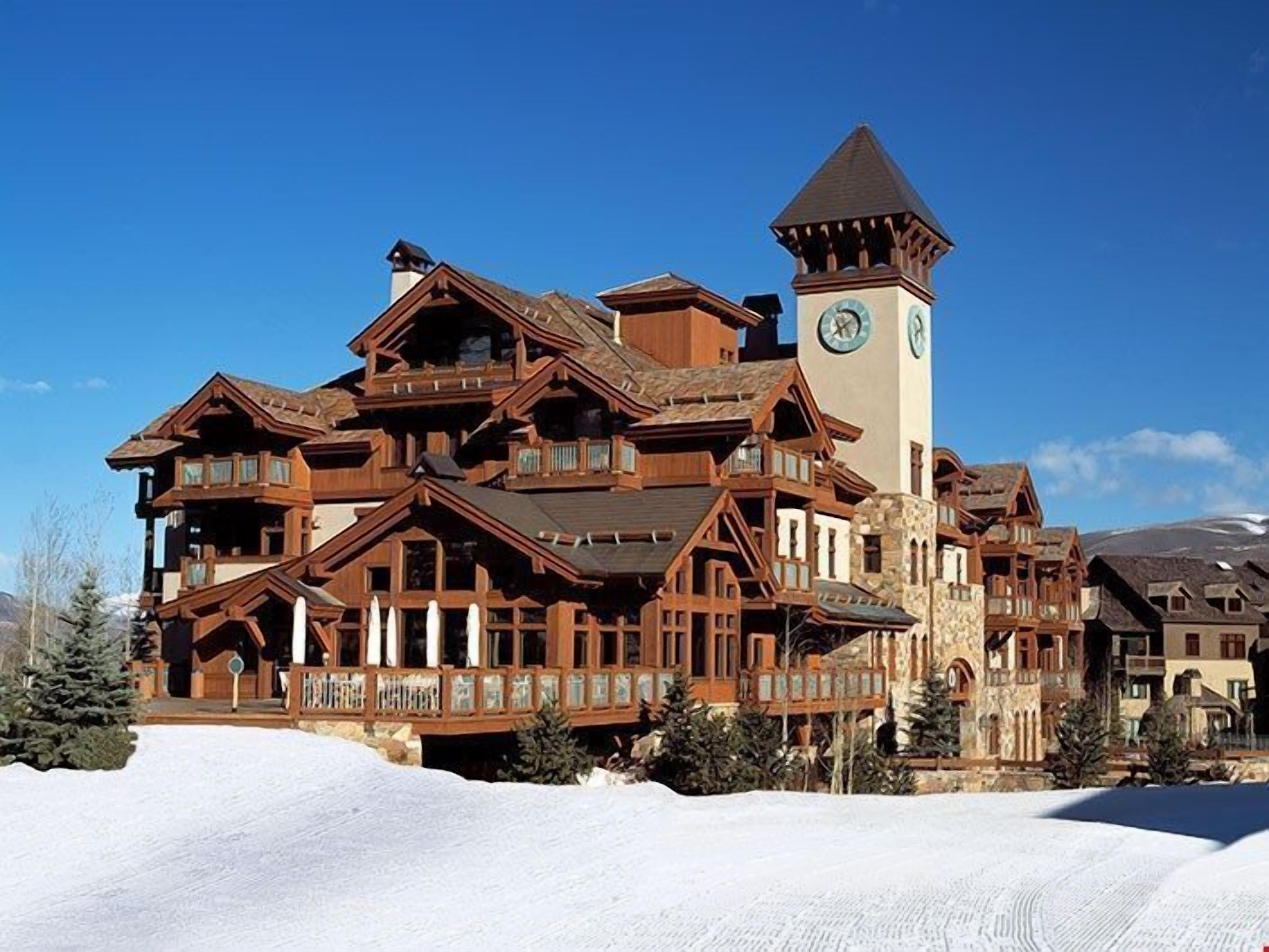 A large, multi-story wooden lodge with a prominent clock tower, surrounded by snow.