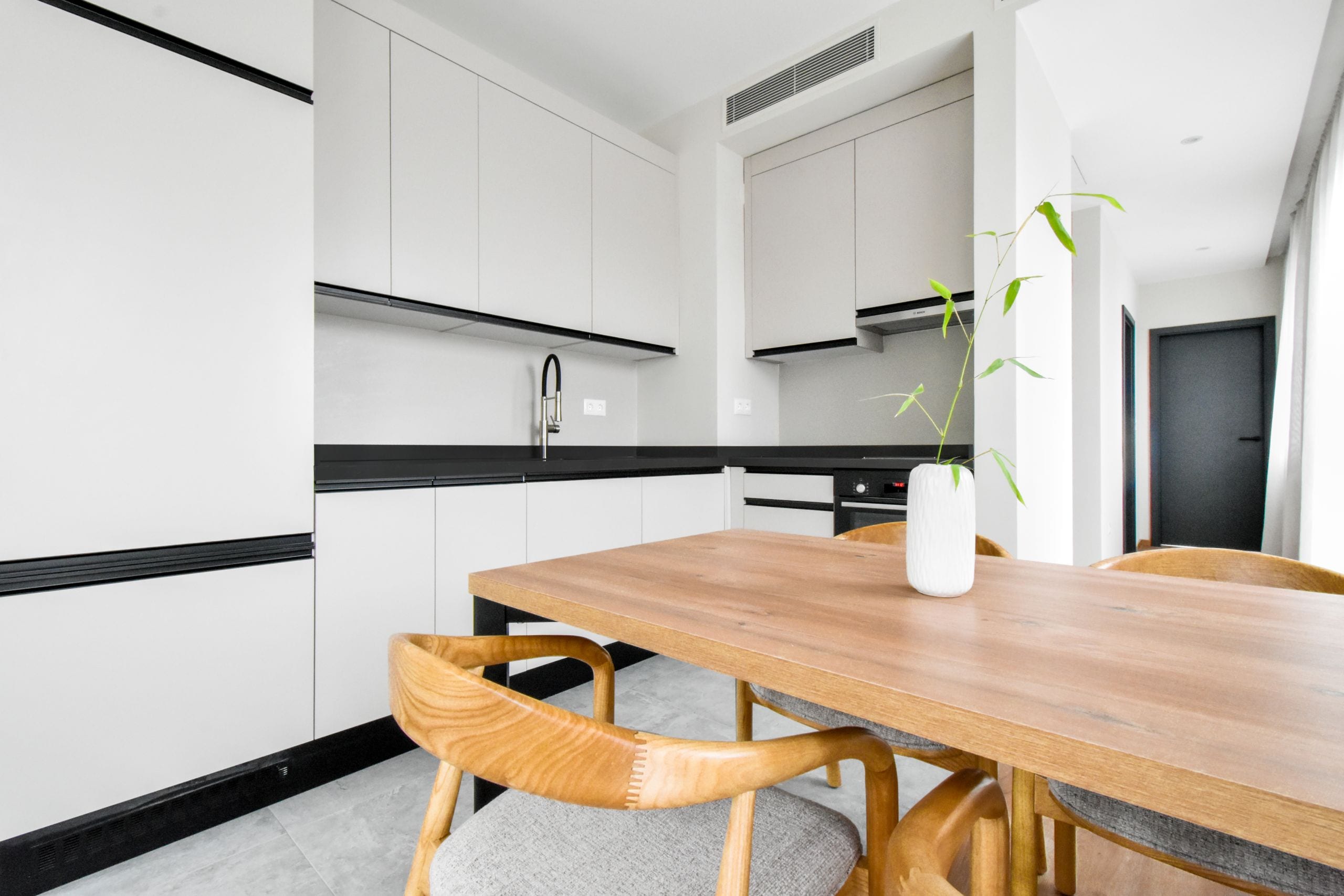 Una cocina moderna con armarios blancos, una mesa de comedor de madera y una planta en maceta.