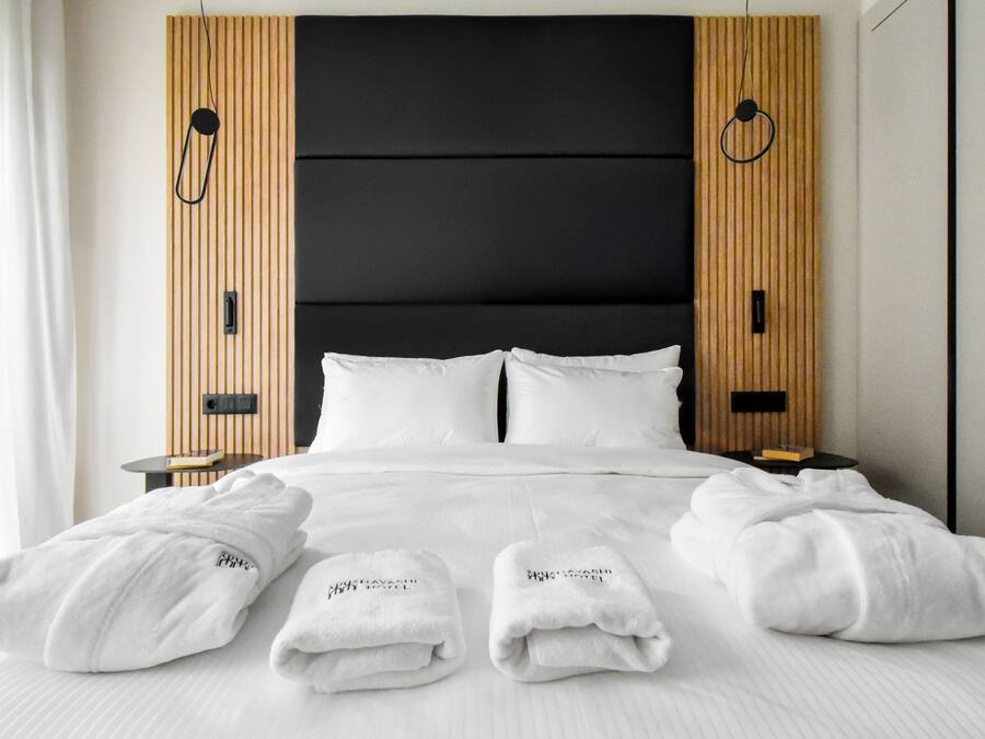 A neatly made bed with white linens and towels, a black upholstered headboard, and wooden paneling on the walls.