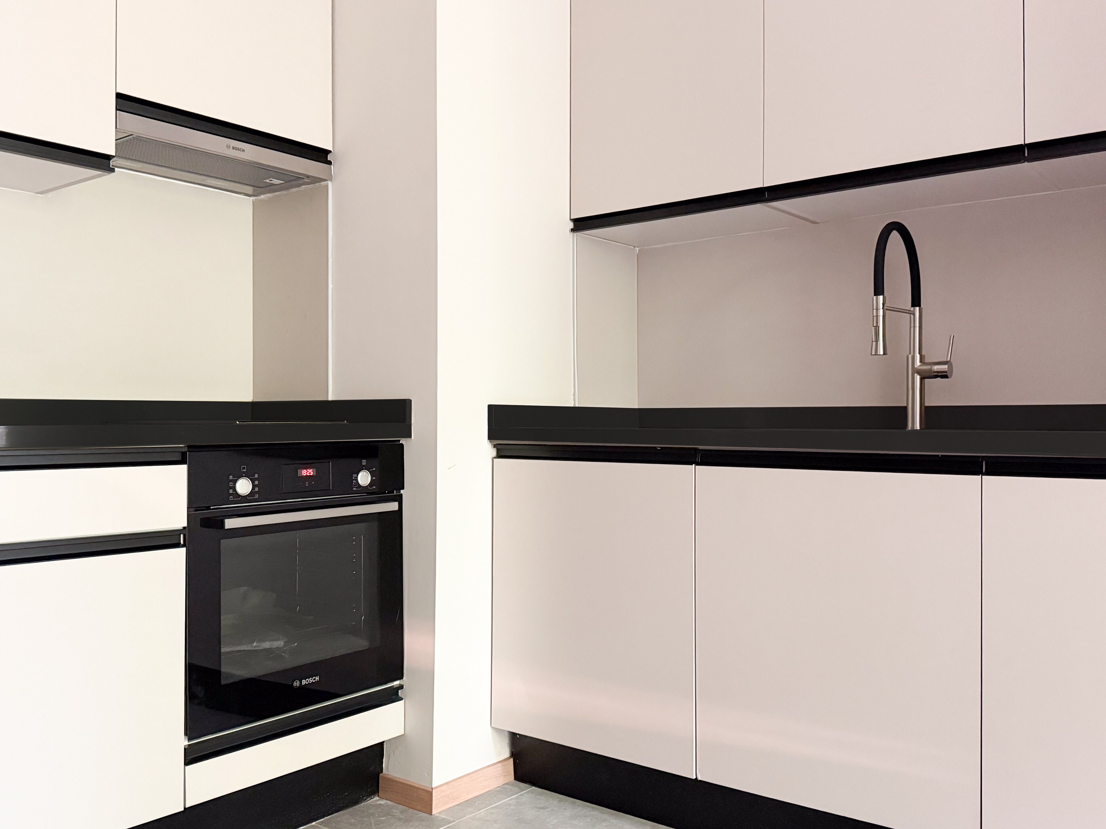 Eine Küche mit Backofen von Bosch, einer schwarzen Arbeitsplatte und weißen Schränken.
