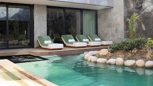 A modern pool area with lounge chairs and a stone wall. -  Hayashi Residence (Sofia)