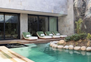 A modern pool area with lounge chairs and a stone wall.