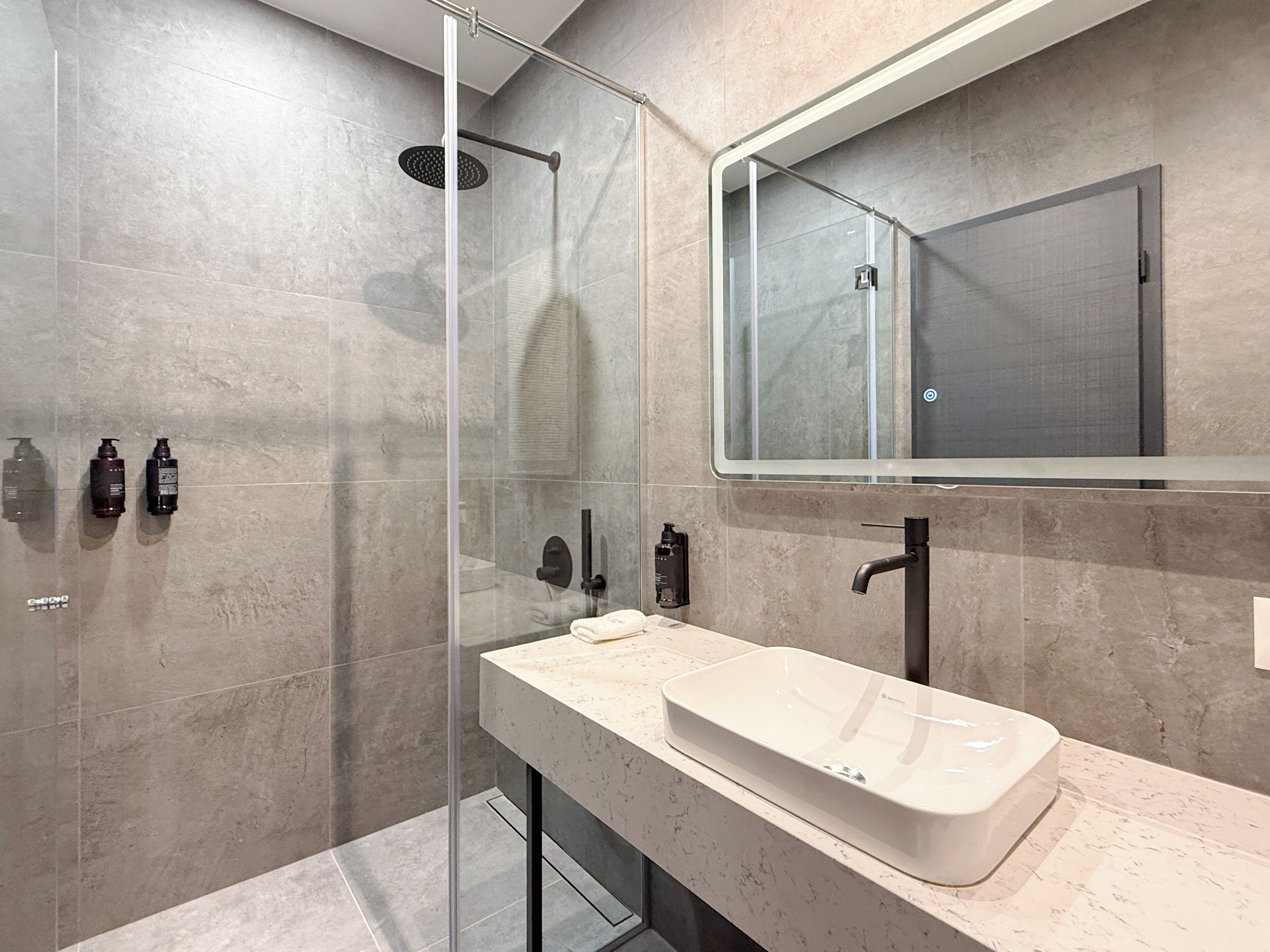 Un baño moderno con ducha envuelta en vidrio, un lavabo blanco y un espejo grande.