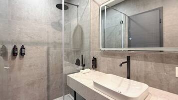 Un baño moderno con ducha envuelta en vidrio, un lavabo blanco y un espejo grande.