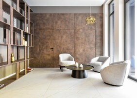 A modern living room with a large bookshelf, two armchairs, a coffee table, and a hanging light fixture.