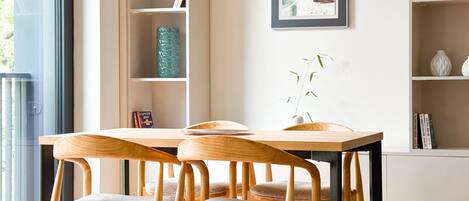 A modern dining area with a wooden table and chairs, a bookshelf, and a framed artwork on the wall.