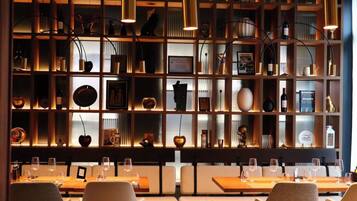 Un restaurante con un ambiente cálido, que presenta una pared de madera con estantes que exhiben varios objetos, y una zona de estar con mesas y sillas.