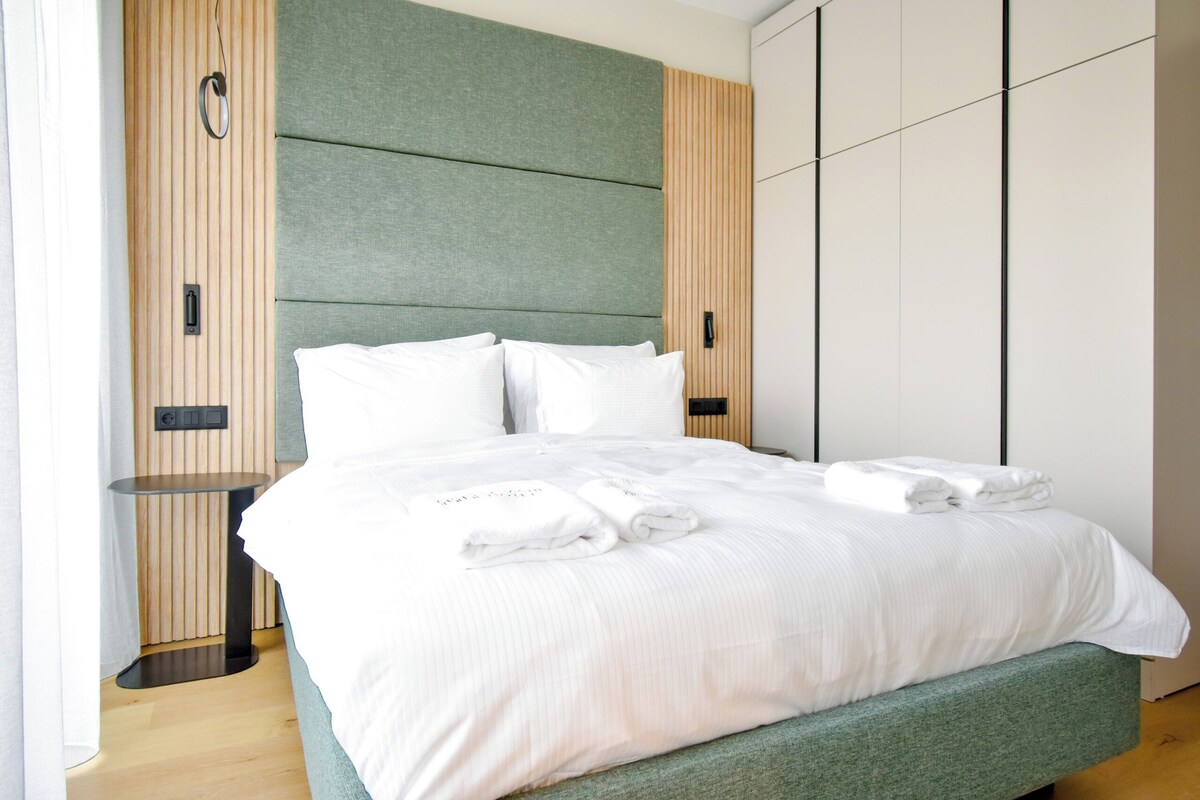 A modern hotel room with a large bed, a small table, and a wardrobe.
