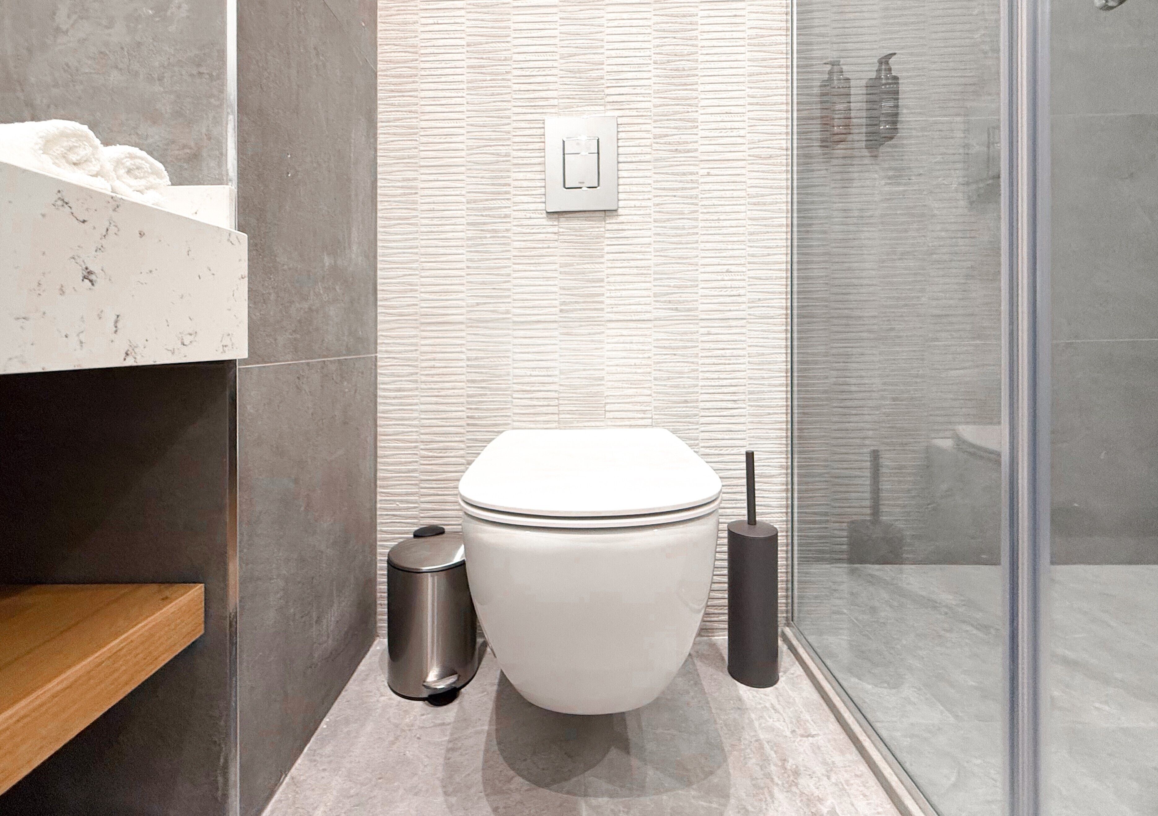 A modern bathroom with a toilet, a trash bin, and a toilet brush.