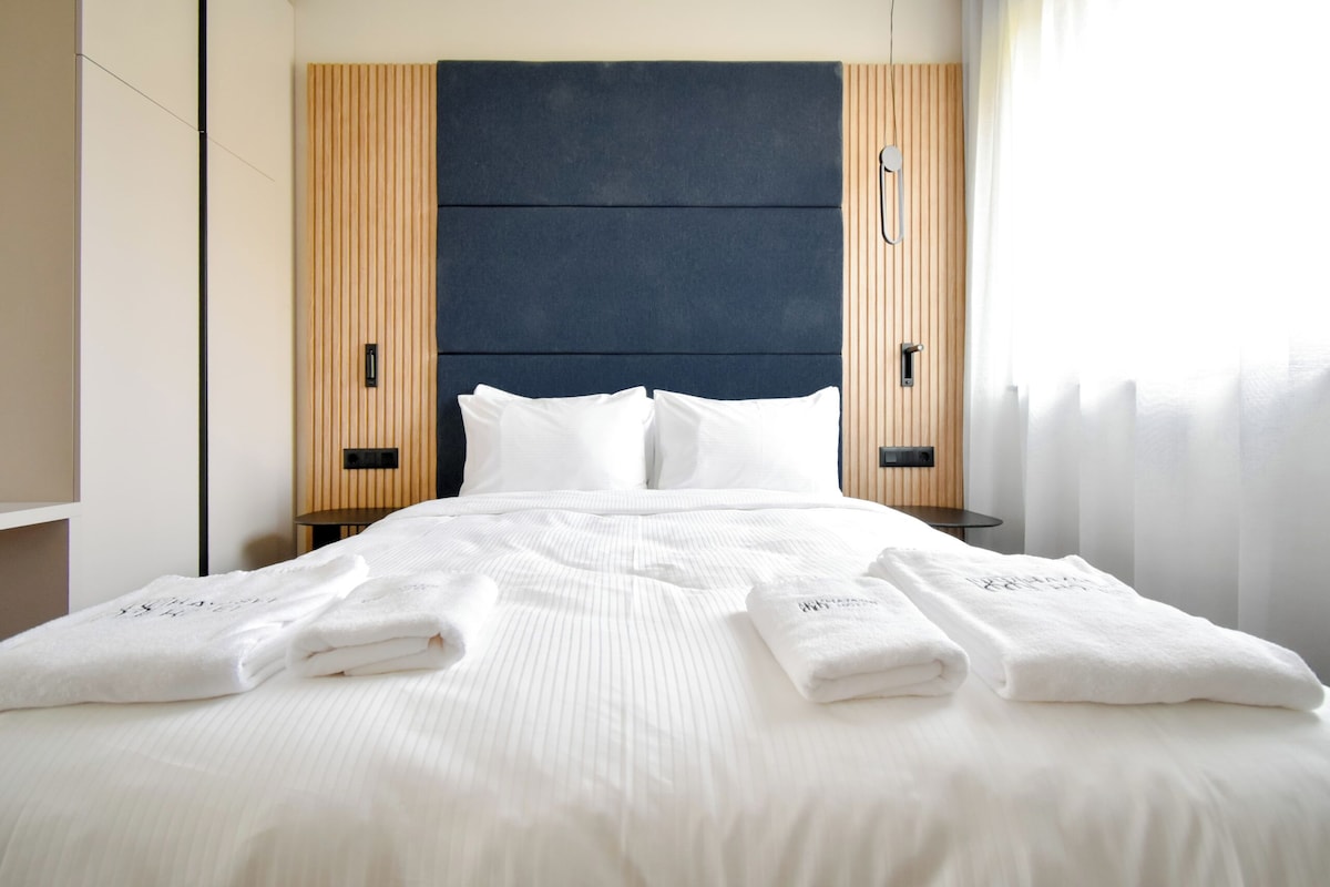 A hotel room with a large bed, two bedside tables, a dark headboard, and wooden paneling on the walls.