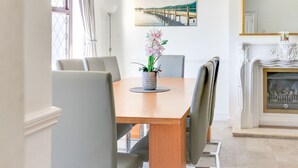 Une salle à manger avec une table en bois, des chaises, un vase de fleurs, un tableau au mur et une cheminée.