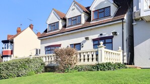 Une maison à deux étages, avec une façade blanche, un toit recouvert de tuiles rouges et un petit jardin à l’avant.
