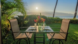 A table set outdoors with chairs, a vase with flowers, and a view of the ocean. - Makani A Kai A6 - On The Beach Steps To The Sand (Maalaea)