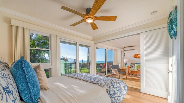 A bedroom with a large bed, a ceiling fan, and a view of the outdoors. - Makani A Kai A6 - On The Beach Steps To The Sand (Maalaea)