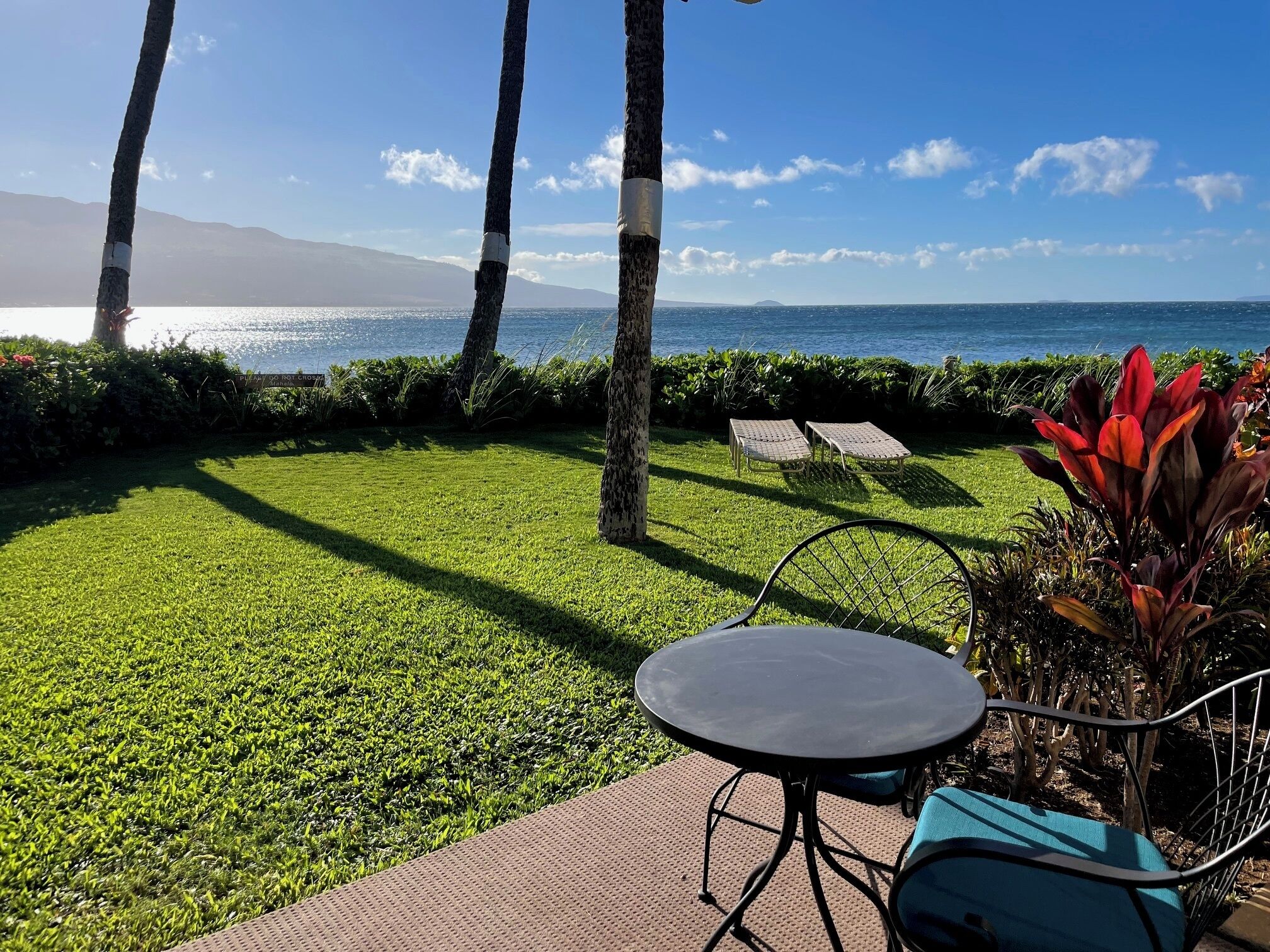 Une terrasse avec une table et des chaises, une pelouse et une vue sur l’océan.