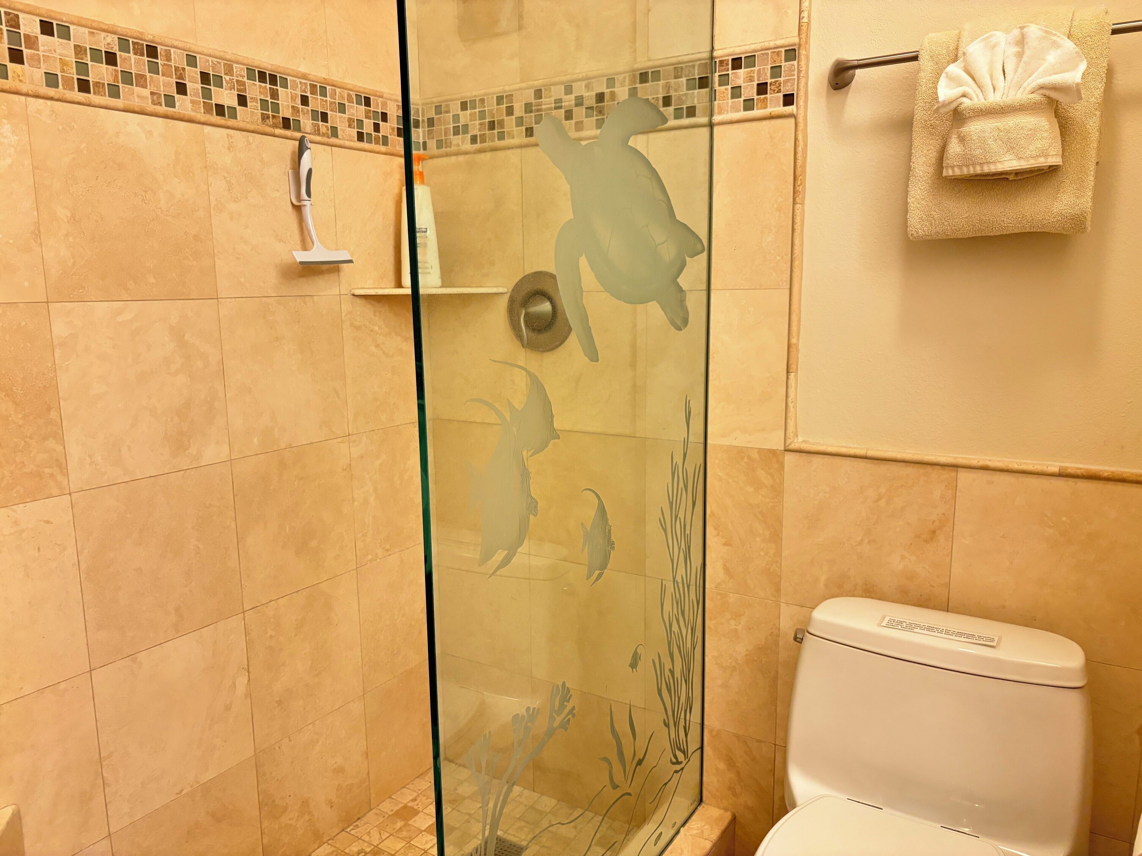 A glass-enclosed shower with a tiled wall, a toilet, and a towel rack with a folded towel.