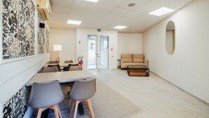 Ein modernes, helles Zimmer mit Esstisch, Stühlen, einer Couch und einem großen Spiegel an der Wand.