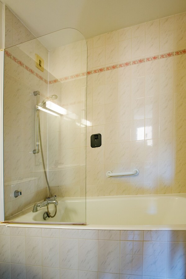 A bathroom with a glass-enclosed shower, a white bathtub, and a handrail. - Gabhouse Lyon Gerland City Living Stay (Vénissieux)