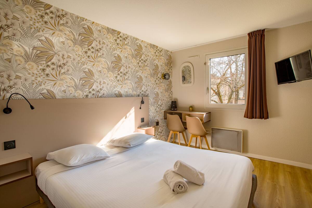 Habitación de hotel con una cama grande, un escritorio con dos sillas, un televisor y una ventana con cortinas.