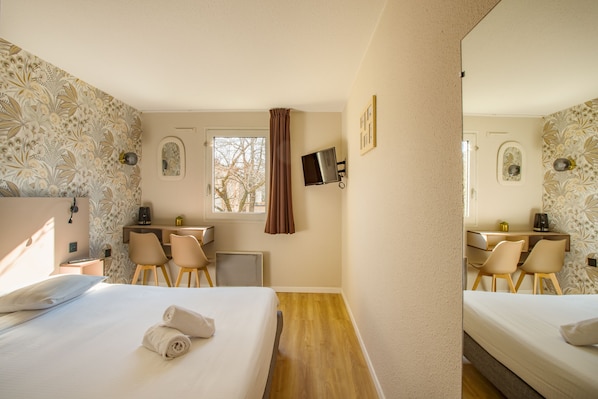 A hotel room with a bed, two chairs, a desk, a TV, and a window with curtains.
