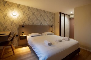 Ein ordentlich eingerichtetes Schlafzimmer mit einem Bett, Nachttischen, einem Schreibtisch und einem Stuhl.