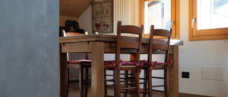 A wooden dining table with four chairs, a radiator, and a window with a wooden frame.