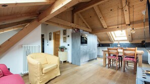 Une chambre confortable située sous les toits, avec un plafond en bois, un lit, une fenêtre et une vue sur la cuisine.