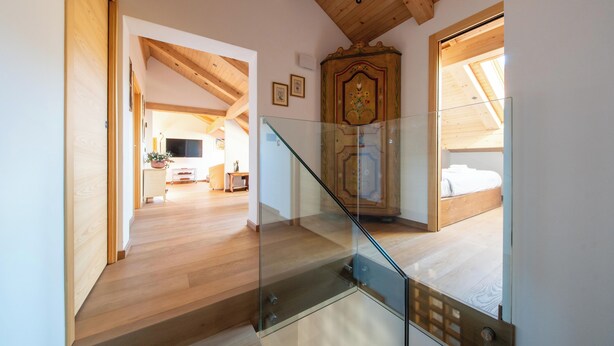 Un escalier avec des rampes en verre menant à une chambre dotée d’un plafond en bois et d’un lit.