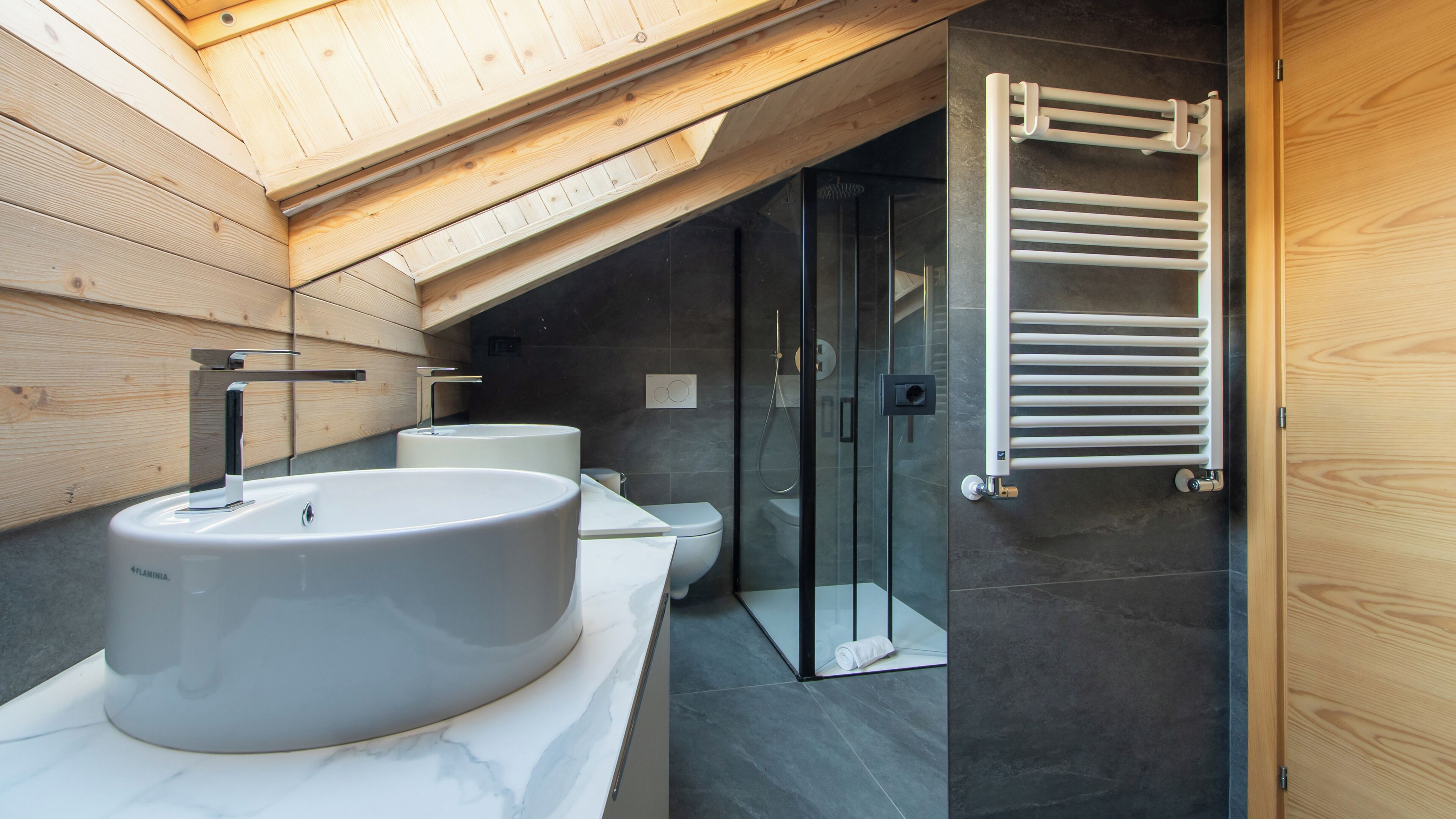 A modern bathroom with a skylight, a large sink, a glass shower enclosure, and a wooden door.