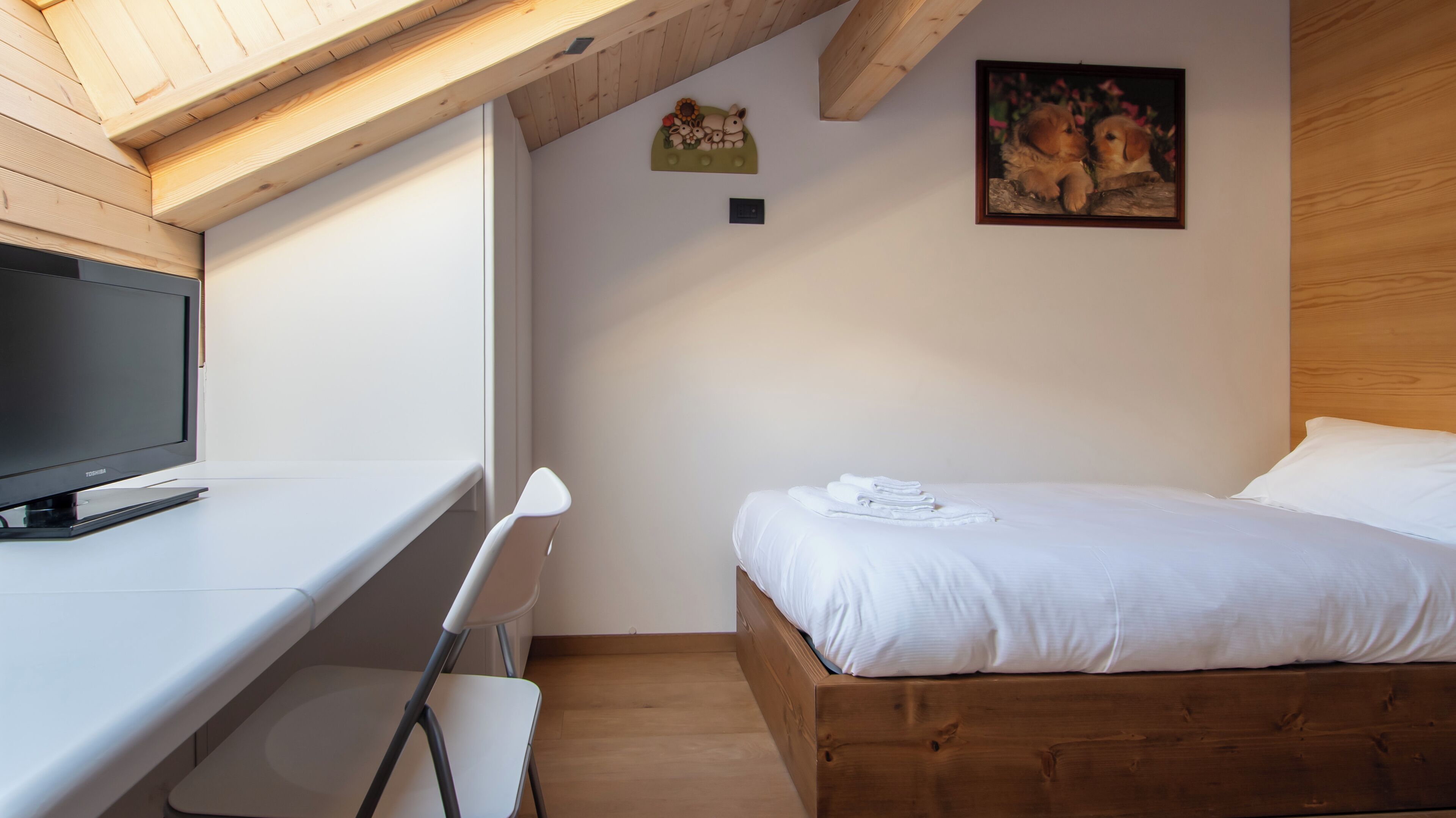 A bedroom with a wooden bed, a white desk with a TV, and a painting on the wall.