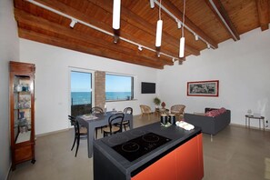 A modern kitchen with a central island, dining area with chairs, and a view of the sea.