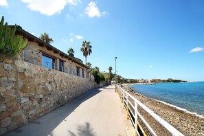 Un paseo marítimo con un muro de piedra, palmeras y cielo azul despejado.