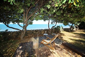A wooden deck with a lounge chair, a small table, and a basket of dried plants, overlooking a body of water.