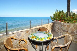 A round table with wicker chairs, a stone wall, and a view of the ocean. - Relais Villa Giovanna -on the sea with garden (Marina di Caronia)