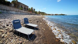 Una spiaggia di ciottoli con due sdraio e un muro in pietra con ringhiera.