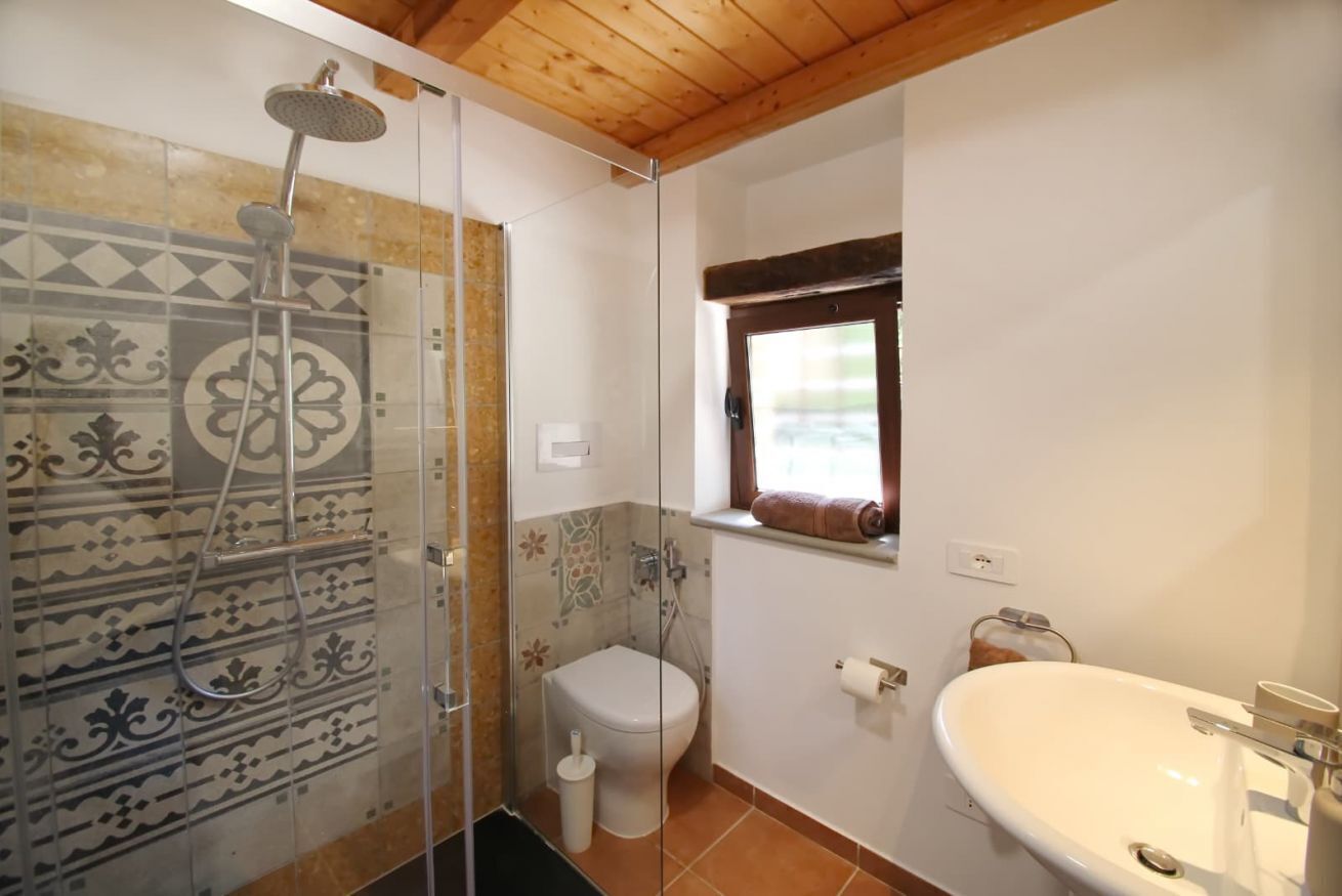 Ein Badezimmer mit Dusche, Toilette und Waschbecken, ausgestattet mit gemusterten Fliesen und einem Fenster.
