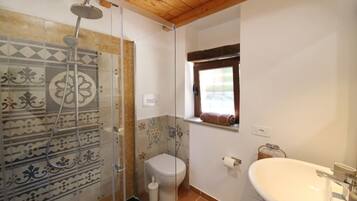 Ein Badezimmer mit Dusche, Toilette und Waschbecken, ausgestattet mit gemusterten Fliesen und einem Fenster.