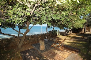 A wooden deck with a view of the sea, a stone wall, and a tree providing shade.
