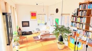 A well-lit living room with a sofa, a coffee table, a bookshelf, and a large window.