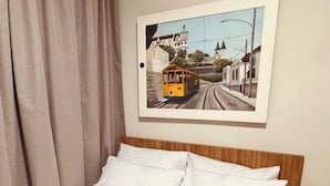 Ein Hotelzimmer mit einem Bett, einem gerahmten Bild einer Straßenbahn an der Wand und einem Fenster mit Vorhängen.