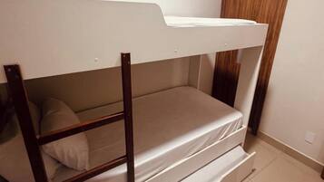 Una cama litera con estructura de madera y ropa de cama blanca en una habitación con suelo de baldosas y puerta de madera.