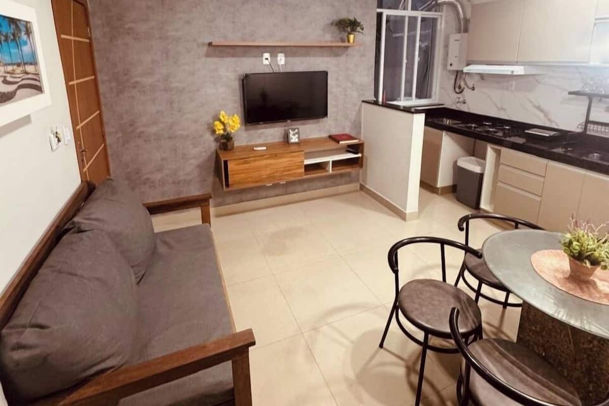Un espace de vie compact comprenant un canapé, un téléviseur, une table à manger avec des chaises, un coin cuisine et un petit balcon.
