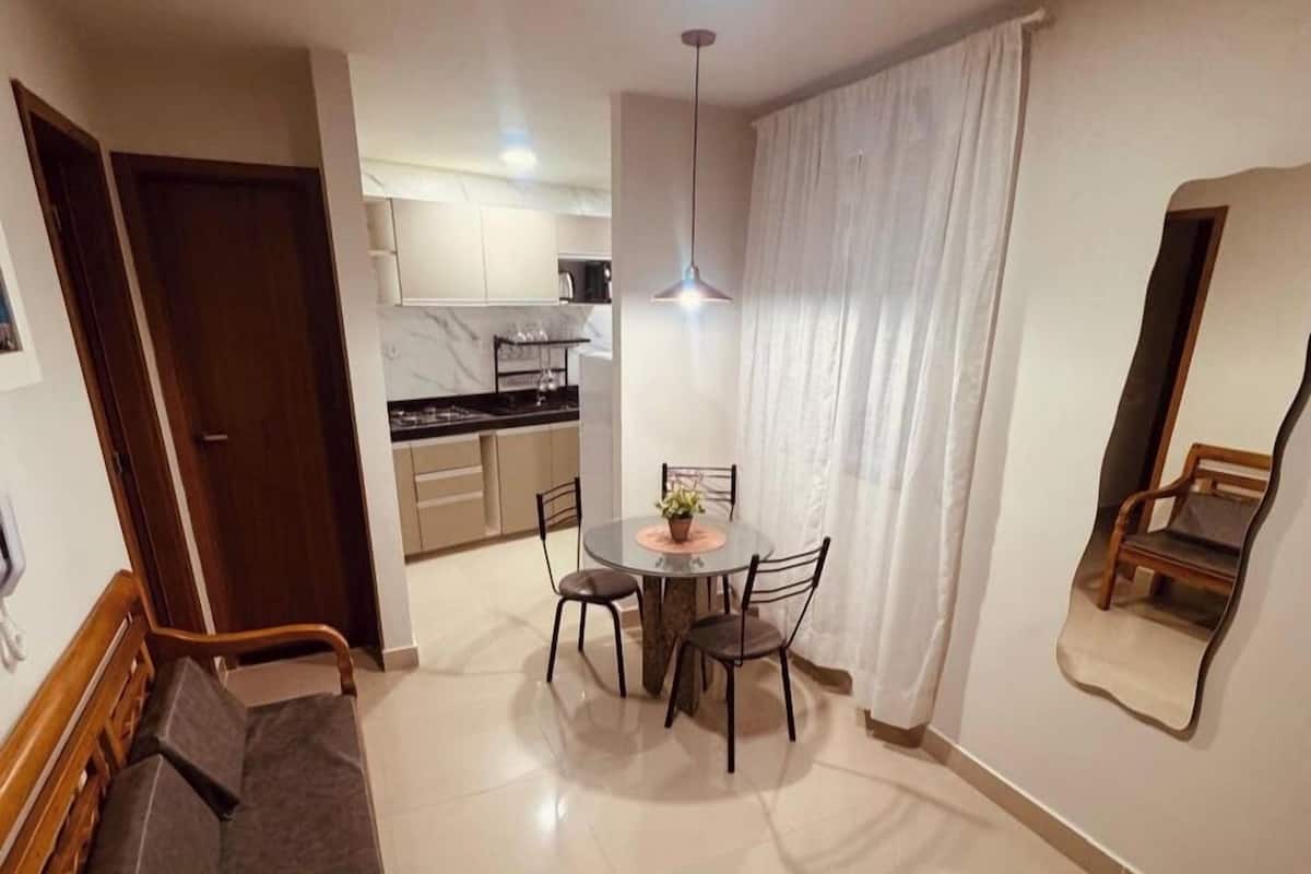 Un salon moderne avec un canapé, une table à manger et des chaises, une cuisine en arrière-plan et un grand miroir au mur.