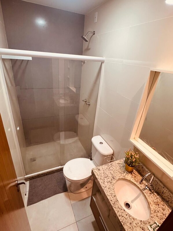 A modern bathroom with a glass-enclosed shower, a toilet, and a granite countertop sink. - Elohim Residencial (Rio de Janeiro)