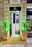 A hotel entrance with a sign reading 'ELOHIM RESIDENTIAL,' potted plants, a doormat, and a tiled floor.